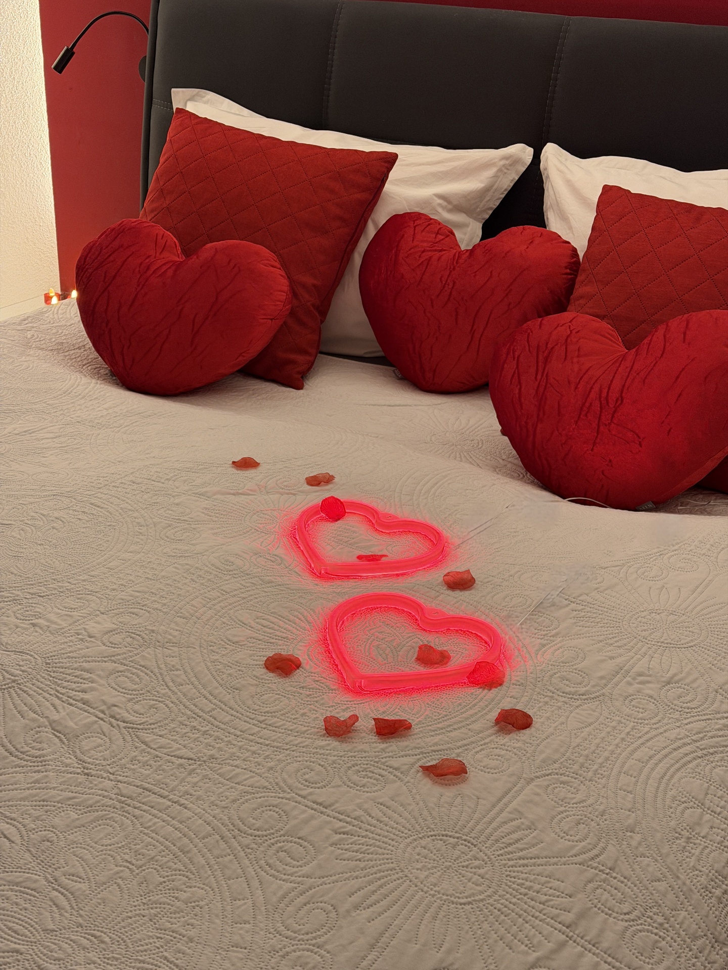 Detailaufnahme der Herzkissen und leuchtenden LED-Herzen mit Rosenblättern auf dem Bett