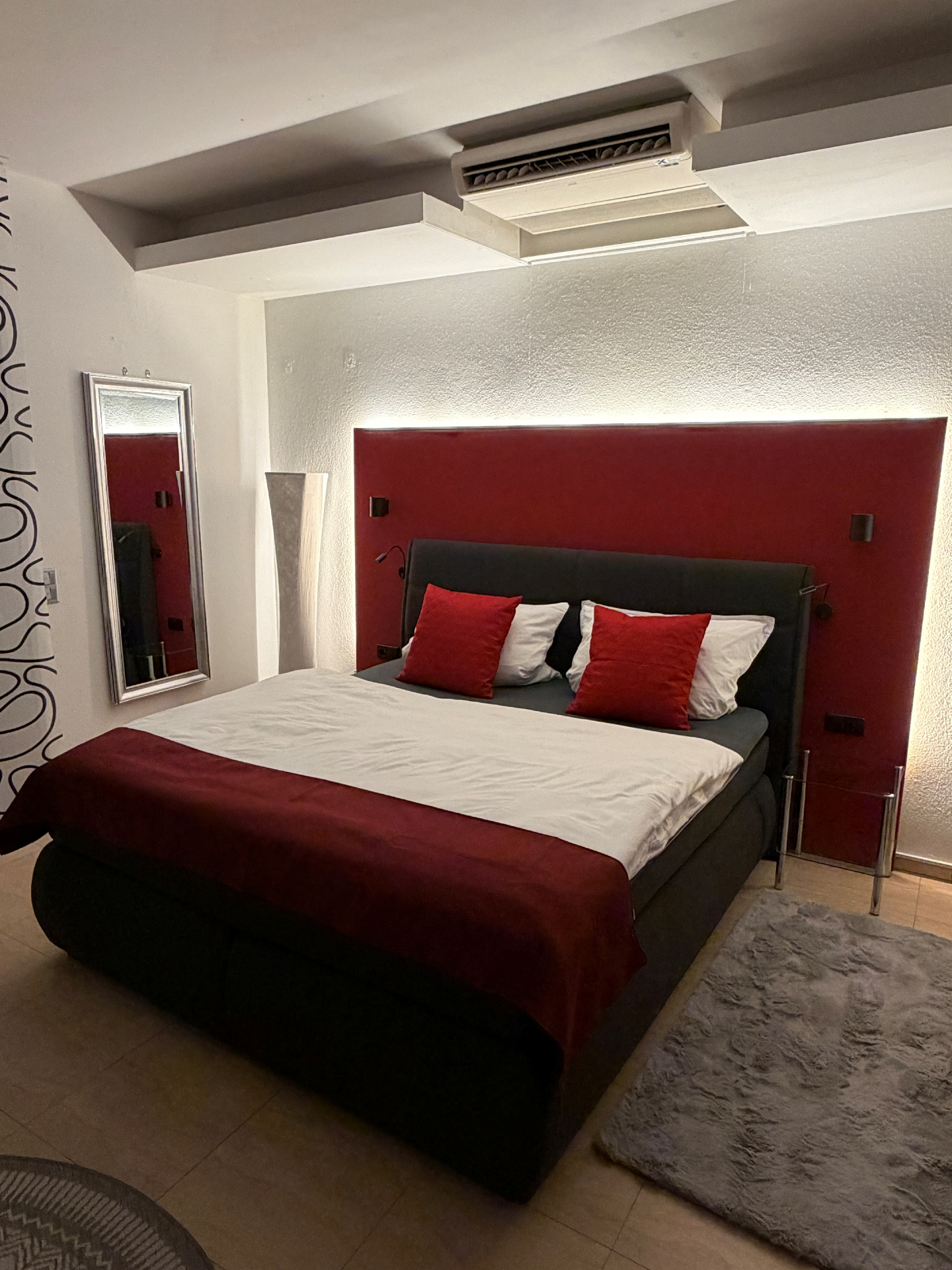 Romantisches Doppelbett mit roter Akzentwand und warmer Beleuchtung